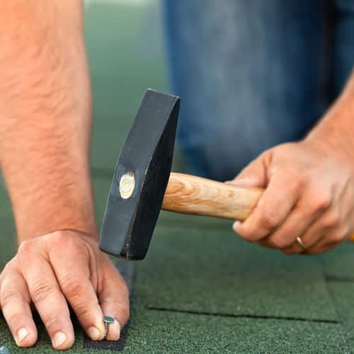 Roofer hammers nail into shingles.